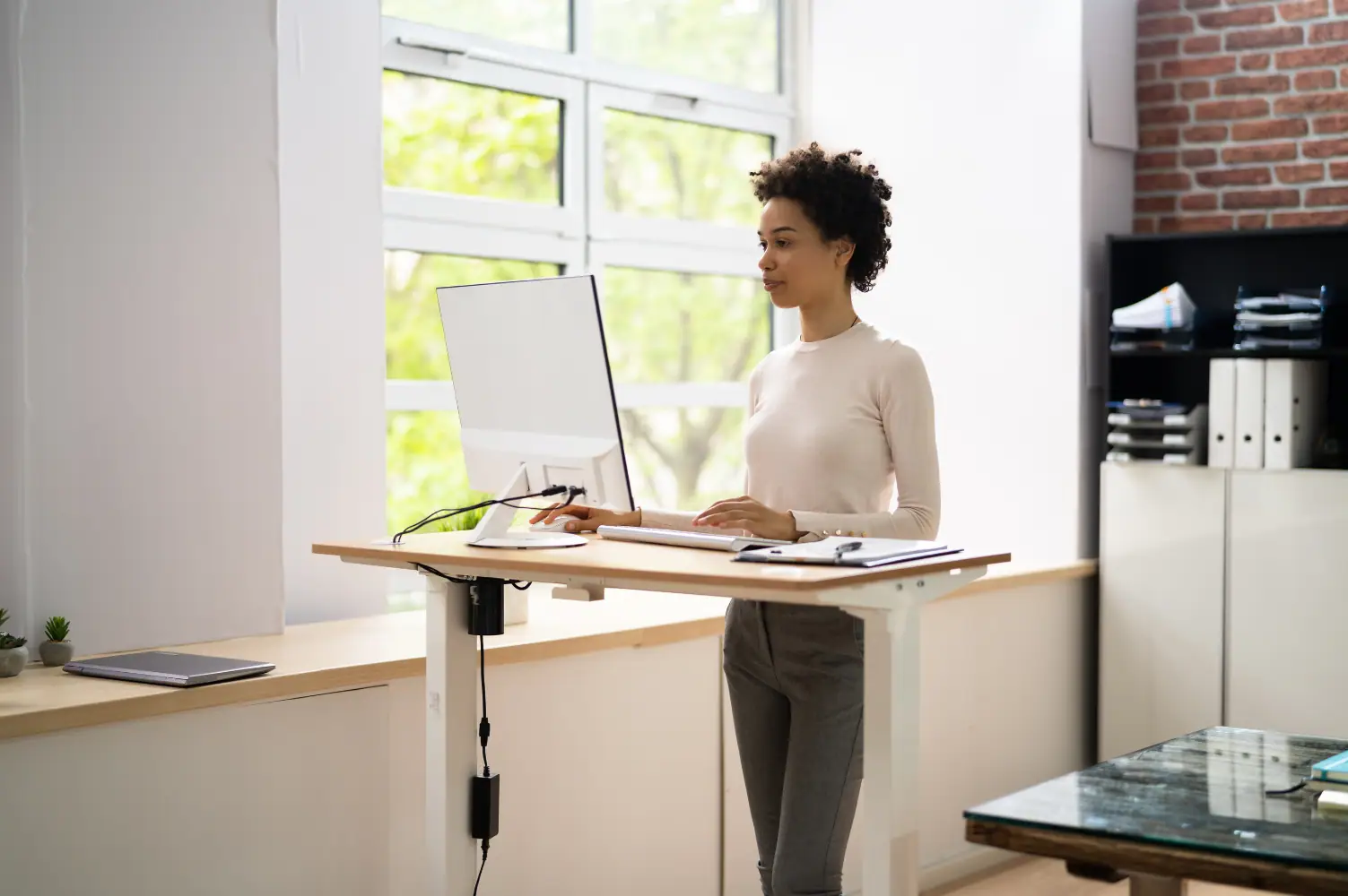 Eine Frau steht an einem höhenverstellbaren ergonomischen Schreibtisch.
